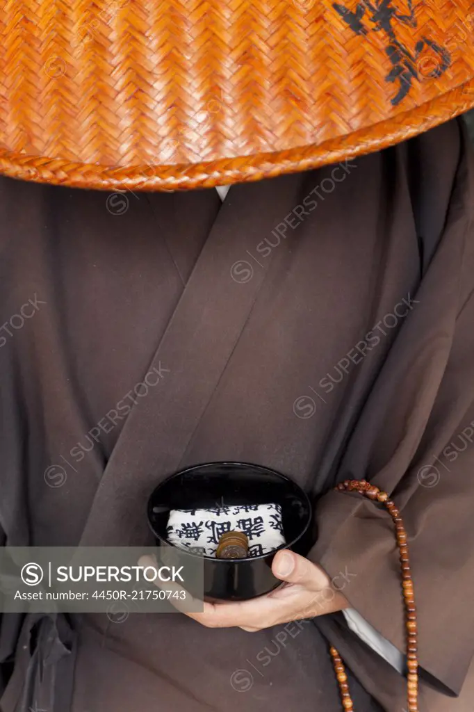 Close up of Japanese monk wearing traditional clothing holding alms bowl.