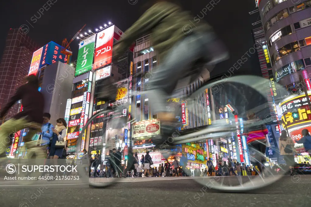 Surface view of cyclists driving on urban street at night illuminated skyscrapers and neon advertising.