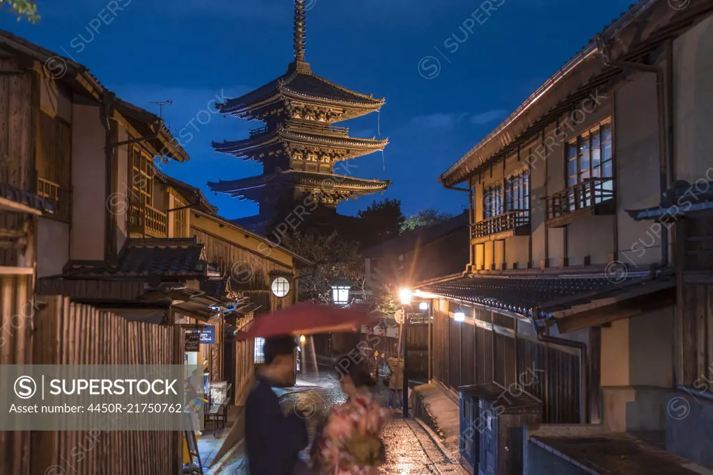 Japanese couple in traditional dress standing in a street at night, a pagoda in the background.