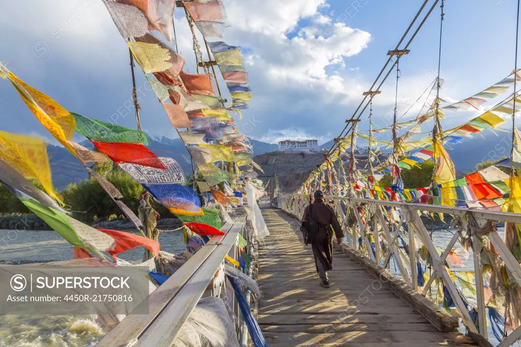 Rear view of man walking across bridge decorated with colourful prayer flags.