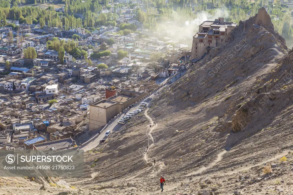 High angle view of town with man climbing up dusty mountain slope.