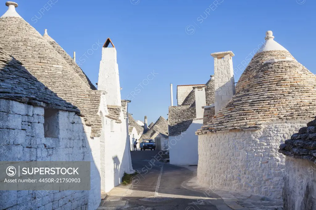 Traditional white washed round stone houses with conical roofs lining Mediterranean street.