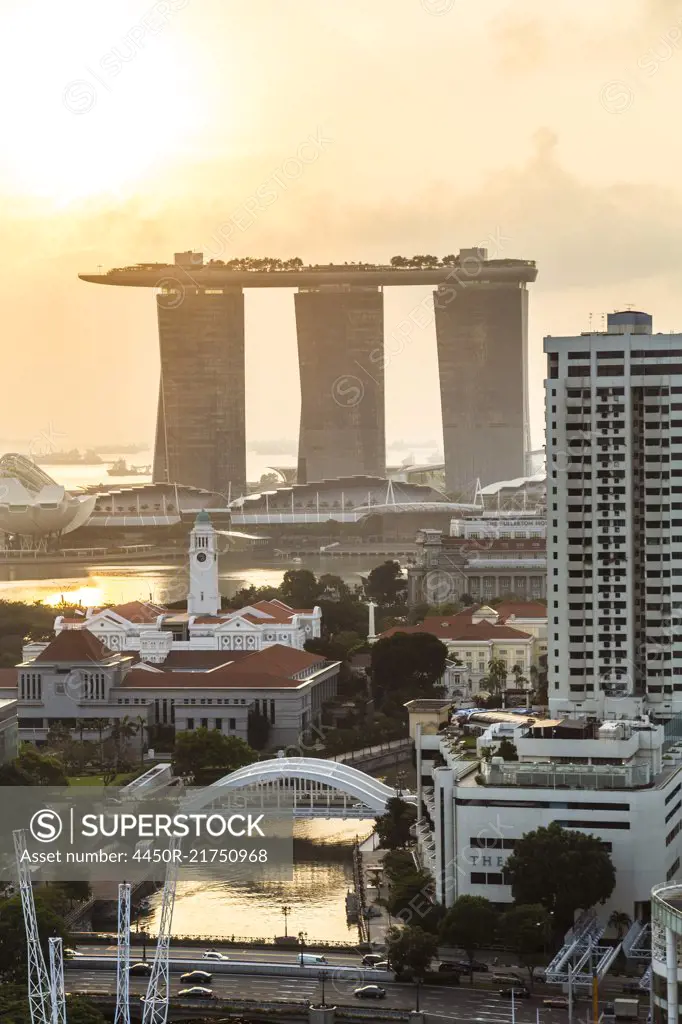 Cityscape with skyscrapers at sunrise, three towers connected by roof terrace in the distance.