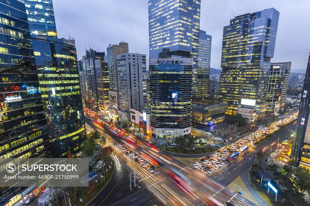 High angle view over city with illuminated skyscrapers, busy street junction and light trails of cars.