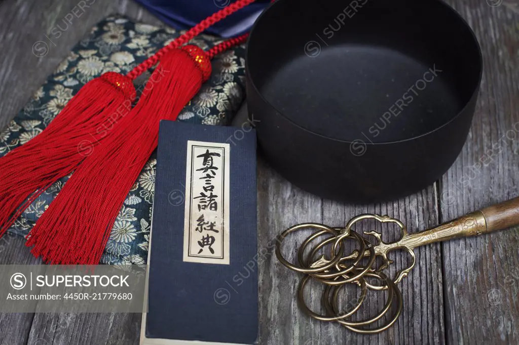 High angle close up of Buddhist prayer text, red silk tassel of a mala and black singing bowl.