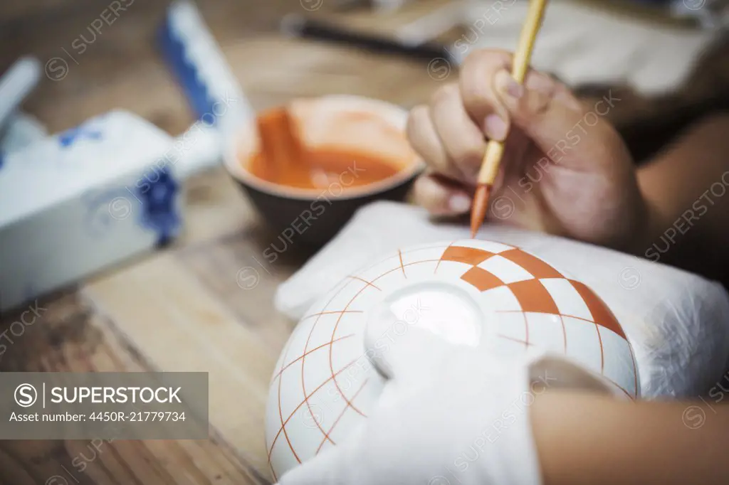 Close up of person working in a Japanese porcelain workshop, painting geometric pattern onto white bowls with paintbrush.