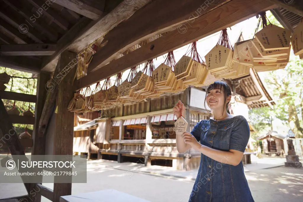 Young woman wearing blue dress looking at wooden fortune telling plaques at Shinto Sakurai Shrine, Fukuoka, Japan.