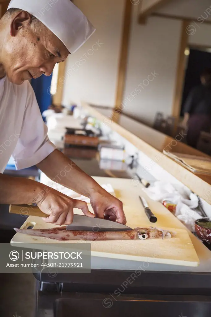 Chef working at a counter at a Japanese sushi restaurant, cutting a squid.