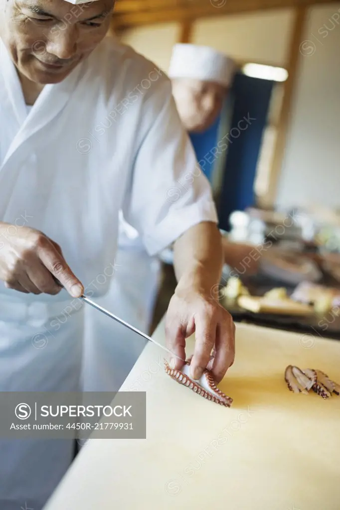 Two chefs working at a counter at a Japanese sushi restaurant, slicing octopus tentacle.