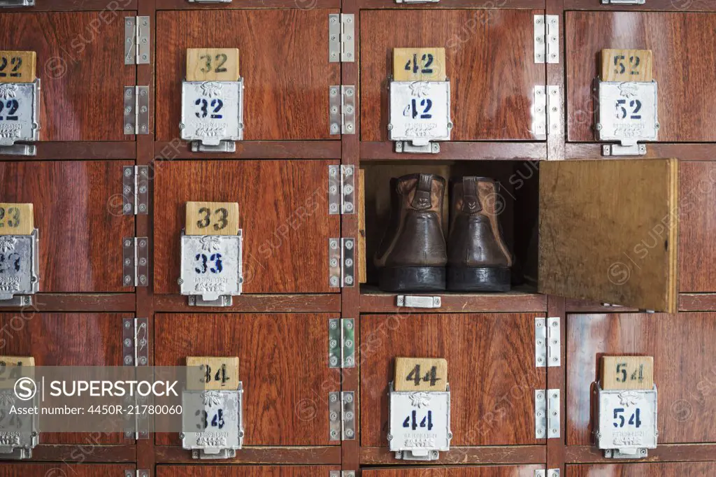 One pair of shoes in a shoe locker with an open door. Lockers in a row, with numbers.