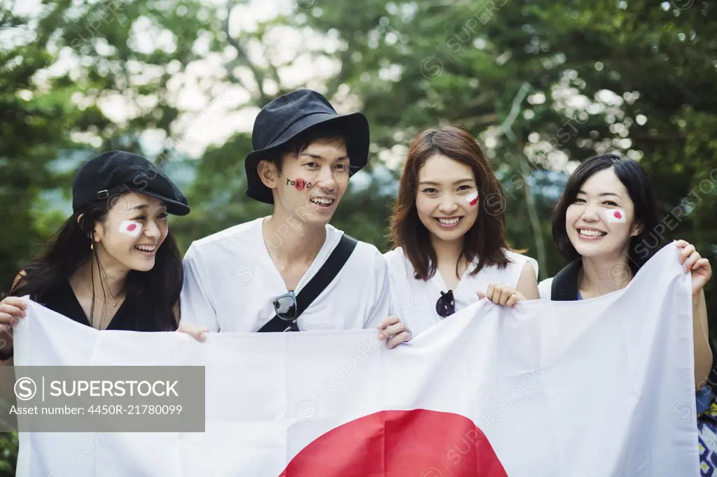 Smiling man and three young women standing outdoors, faces painted, holding Japanese flag.