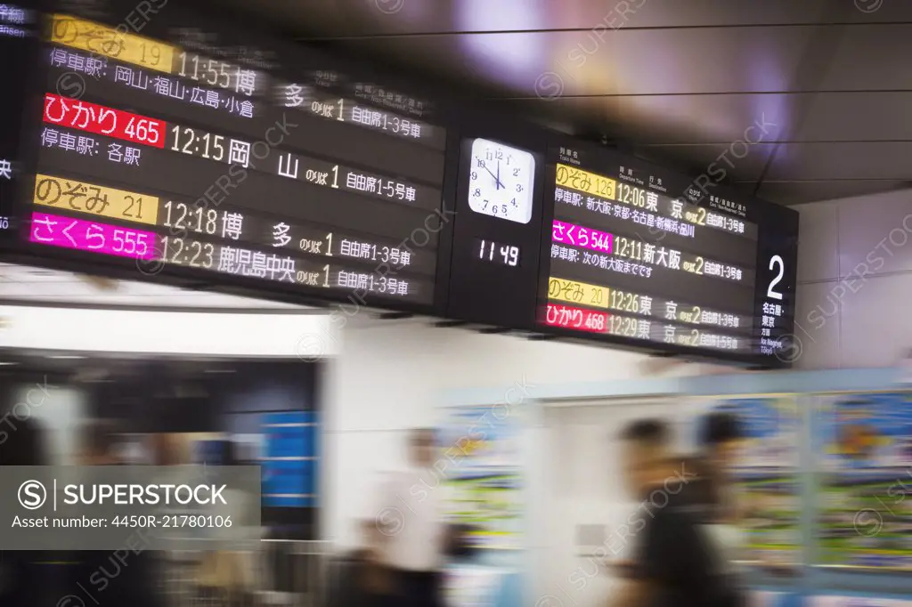 Close up of illuminated departure board with clock at a Japanese train station.