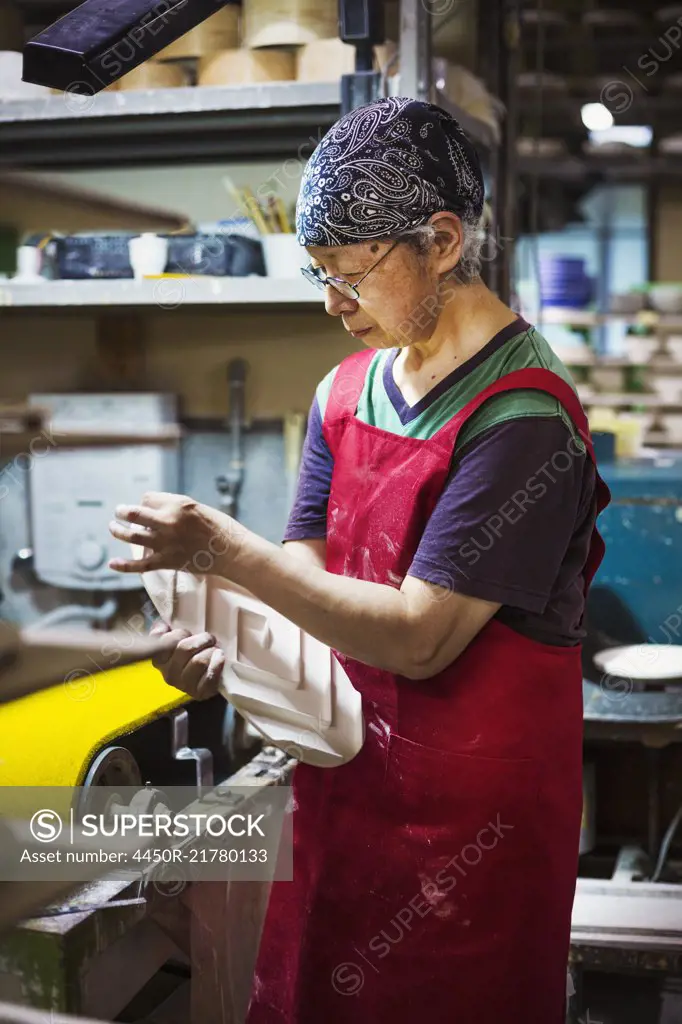 Woman working in a Japanese porcelain workshop, wearing apron, holding white porcelain object.