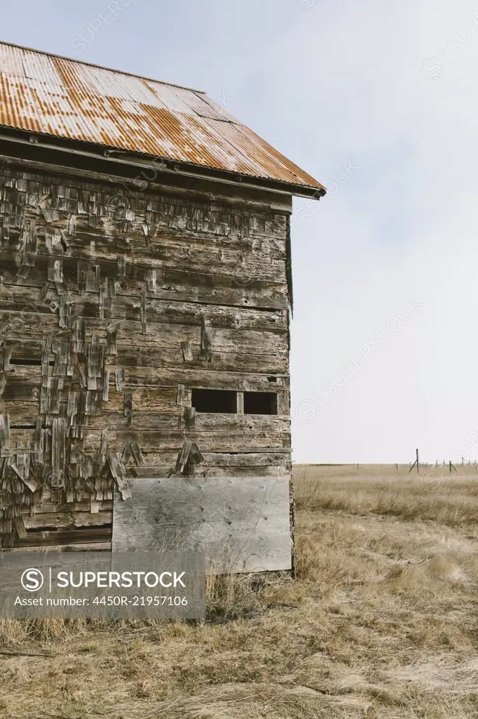 An old abandoned farmhouse with wooden shingle tiles on the walls. Silvery grey colours.