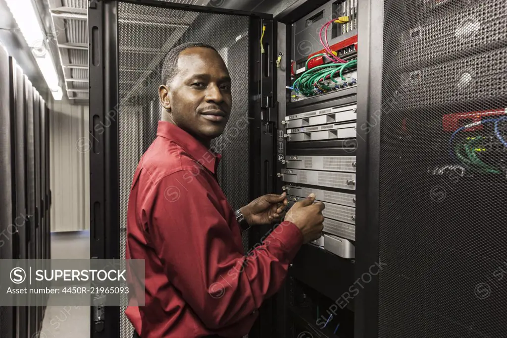 Black man technician working on computer servers in server farm.