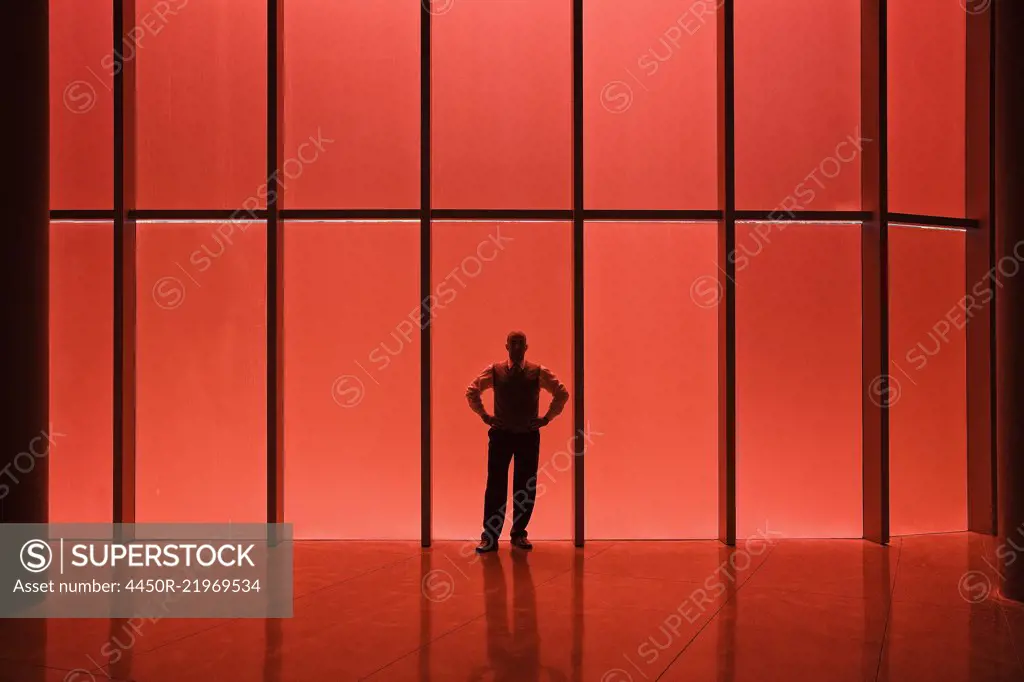 Businessman standing next to red tinted windows in an office lobby.