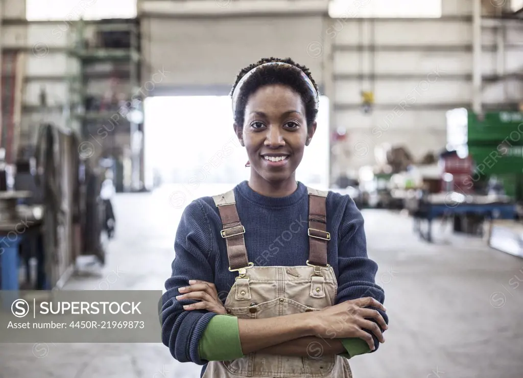 Black woman factory worker wearing coveralls in a large sheet metal factory.