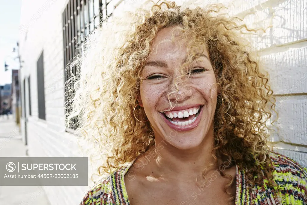 Portrait of young smiling woman with long curly blond hair, looking at camera.