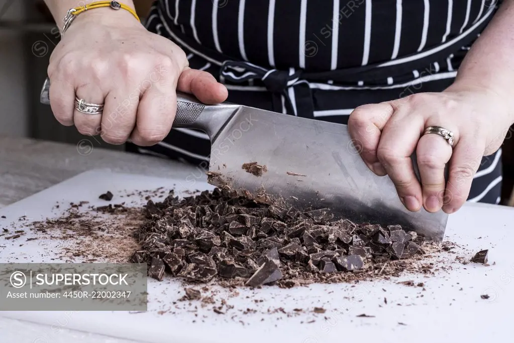 A cook chopping chocolate pieces with a large cleaver.