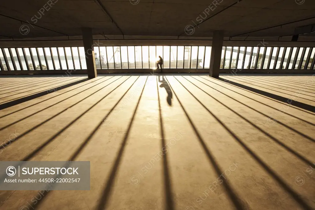 Businessman exploring new empty raw business space for a new office at sunset, sunlight streaming through the wall of glass.