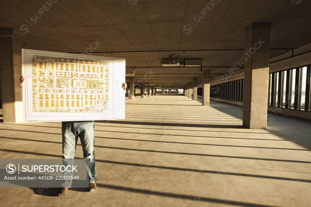 Businessman holding up plans for new office space standing in the middle of the empty raw space.