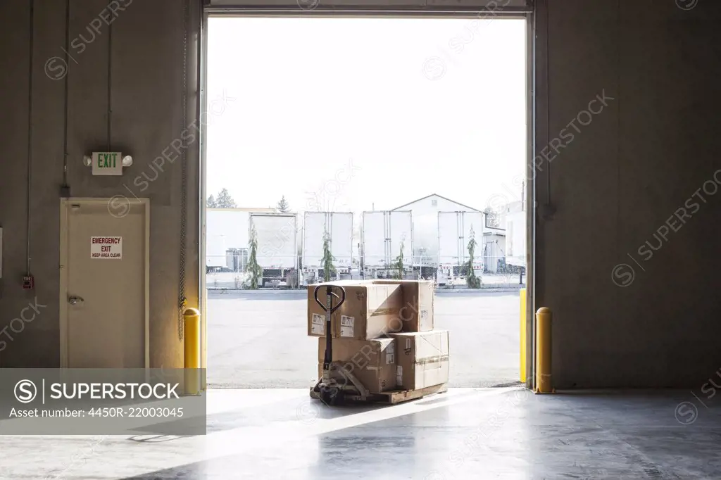 A small stack of products in boxes sitting on a manual pallet jack in a loading dock door at a distribution warehouse.