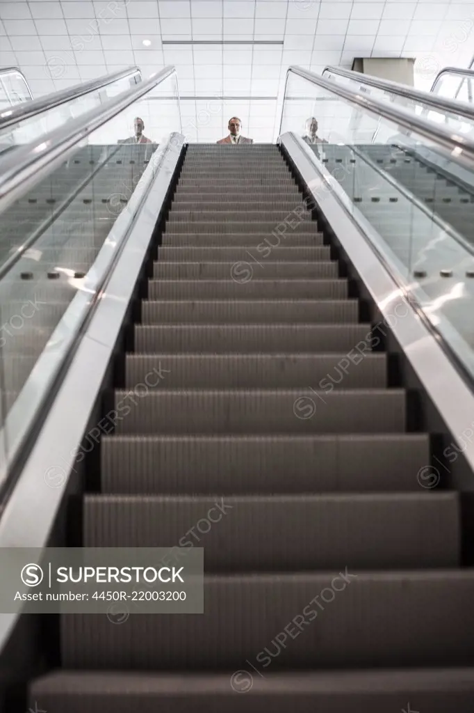 Looking up an escalator with a person about to get on the escalator in a convention center space.