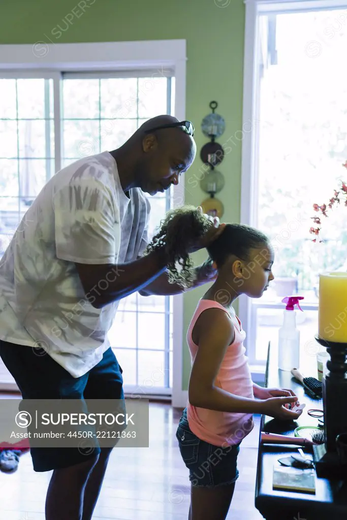 Dad fixing his daughter's hair, holding it and plaiting it.