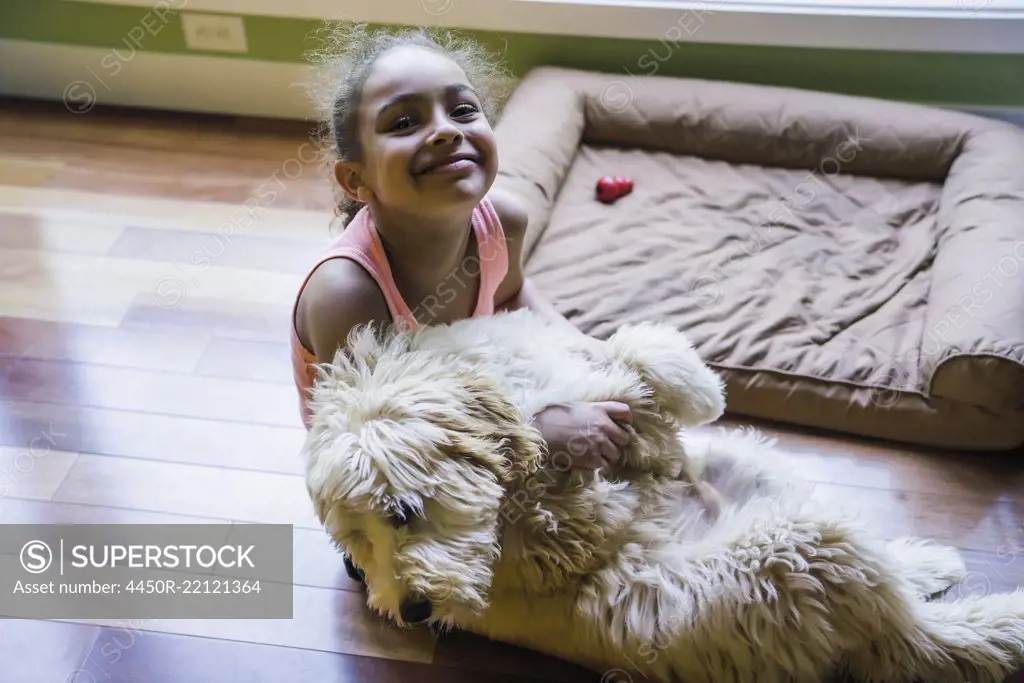 Smiling girl sitting on floor hugging labradoodle puppy