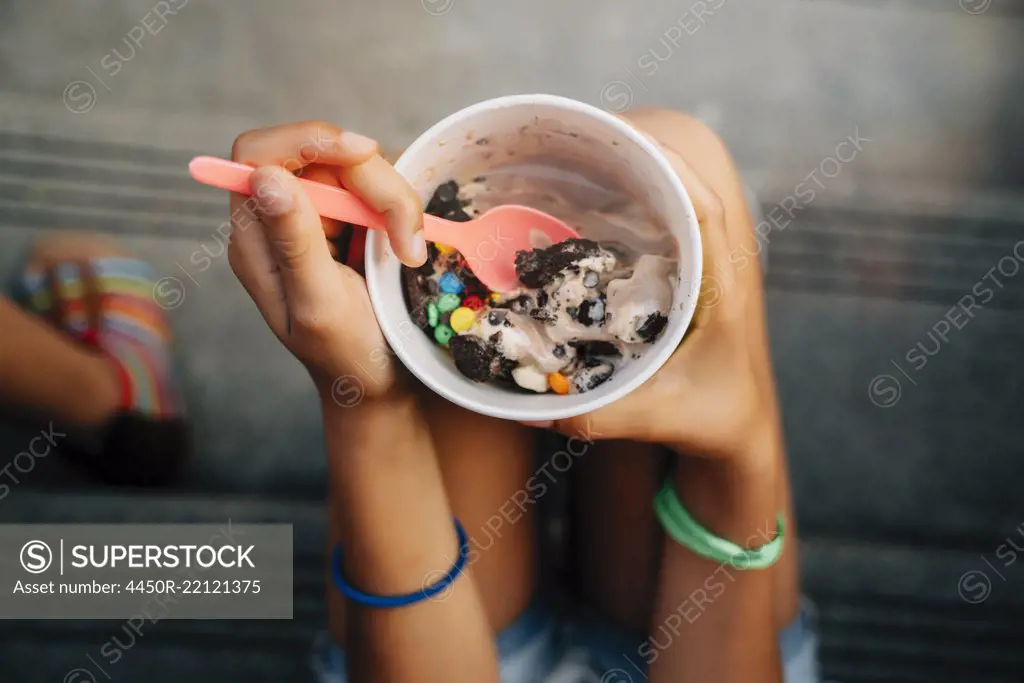 High angle close up of girl sitting on steps eating ice cream