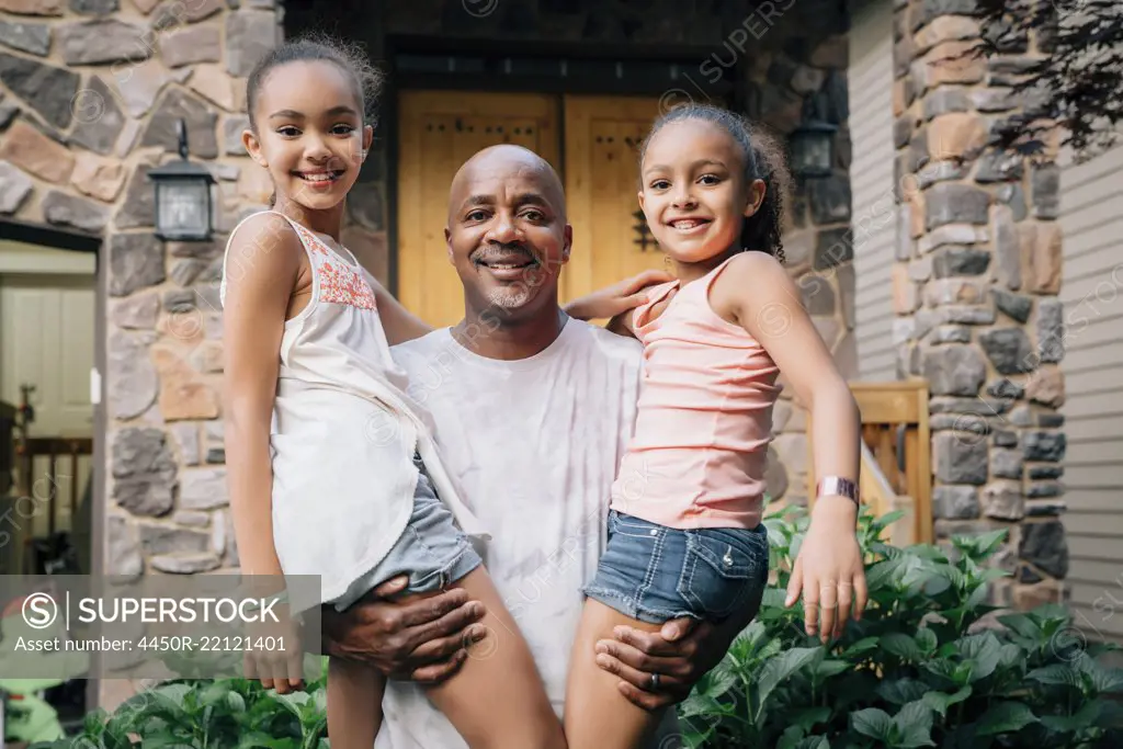 Portrait of happy dad hugging daughters in front of house