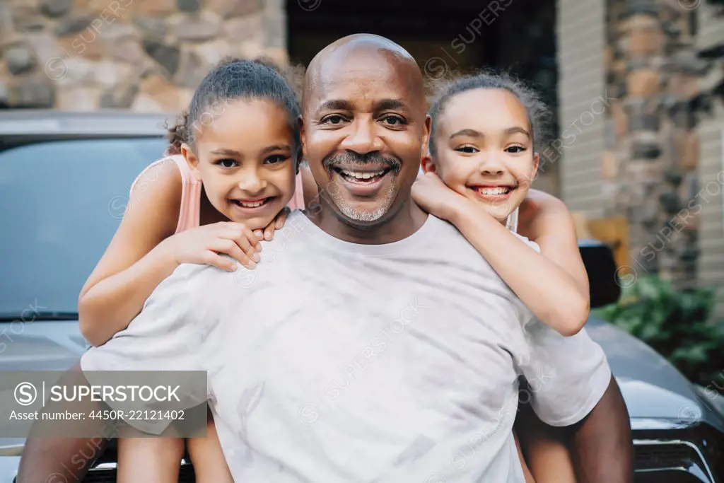 Portrait of happy dad hugging daughters in front of house