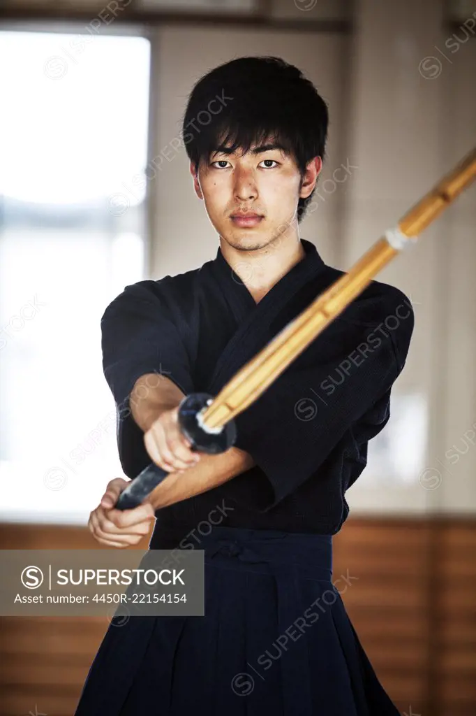 Male Japanese Kendo fighter holding wood sword in combat pose, looking at camera.