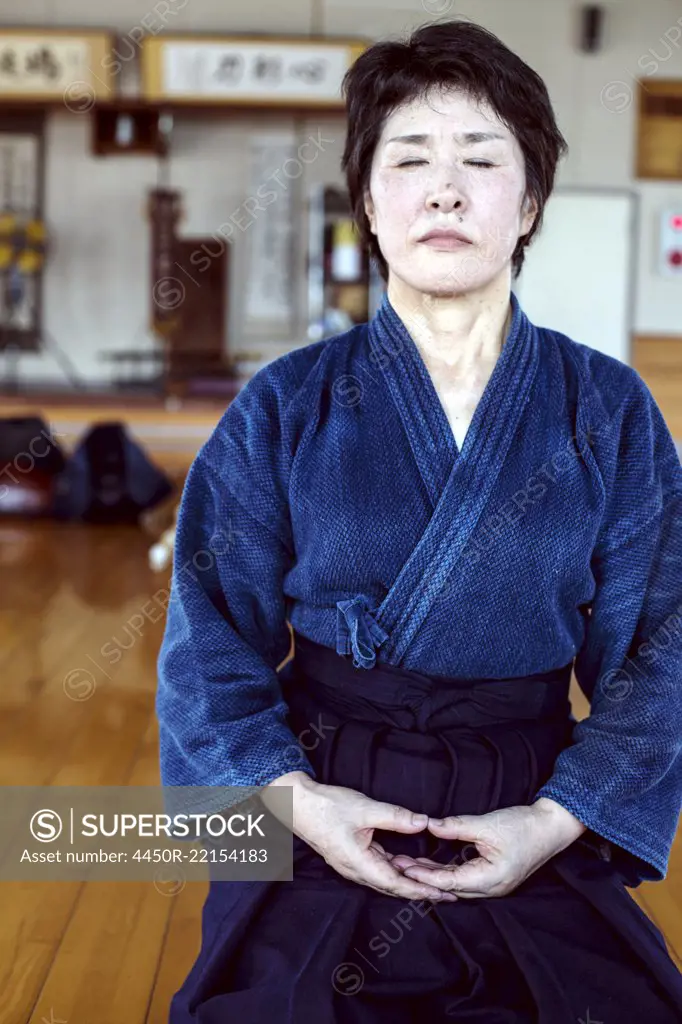 Female Japanese Kendo fighter kneeling on wooden floor, meditating.