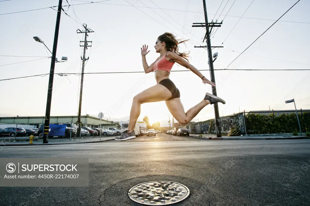 Female athlete running along street at dusk.