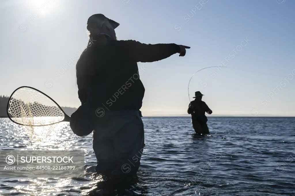 A guide advises his client while fly fishing in salt water for searun coastal cutthroat trout and salmon in northwest Washington State, USA