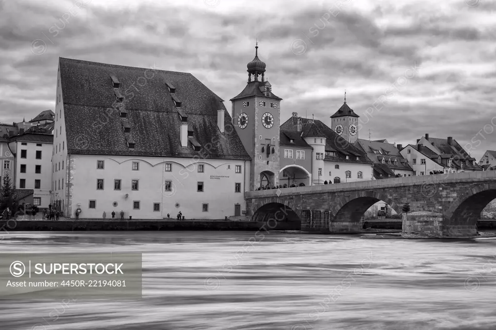 Medieval stone arch bridge over the Danube river with historic buildings and city gate, Regensburg, Germany.