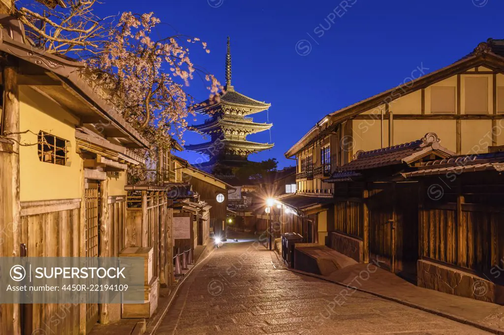 Traditional houses lining a narrow street with a pagoda in the distance, Higashiyama at night, Kyoto, Japan.