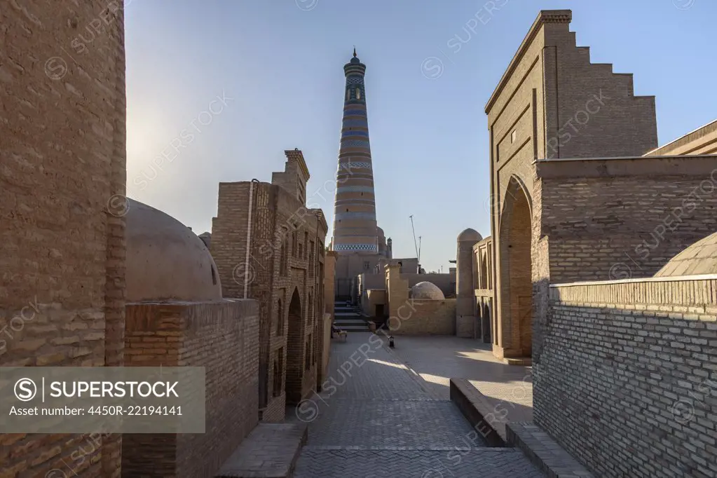 Sunrise, a narrow street of brick buildings and a view of a tall round brick built minaret in Khiva, Uzbekistan.