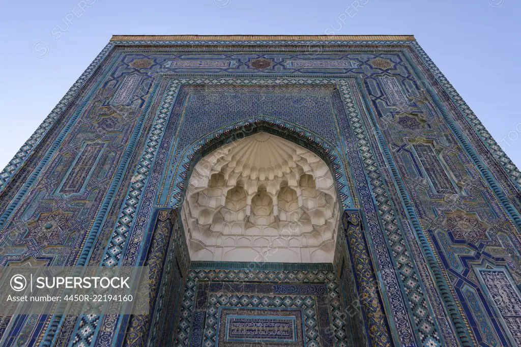 Registan square in Samarkand, a huge arch covered in glazed patterned tiles, blue white and golden, and a carved dome.