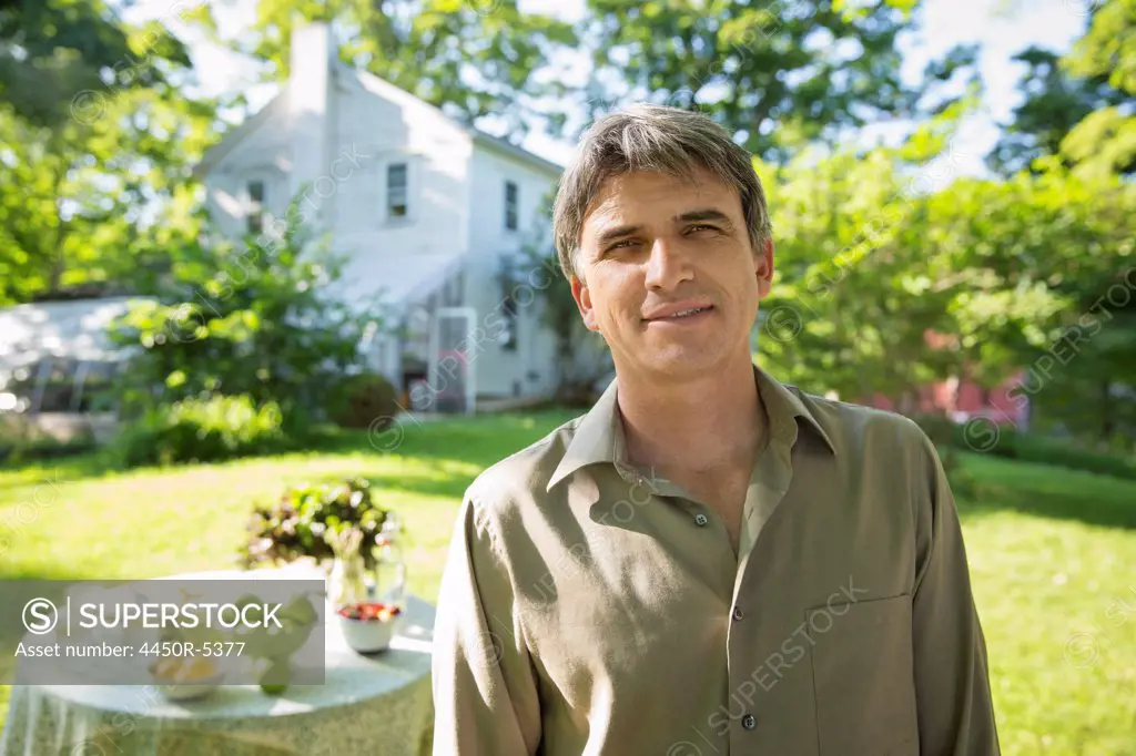 Outdoors in summer. On the farm. A man in a farmhouse garden, beside a round table with fresh lemonade drinks.