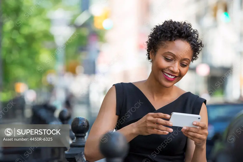 People on the move. A woman in a black dress on a city street, checking her phone.