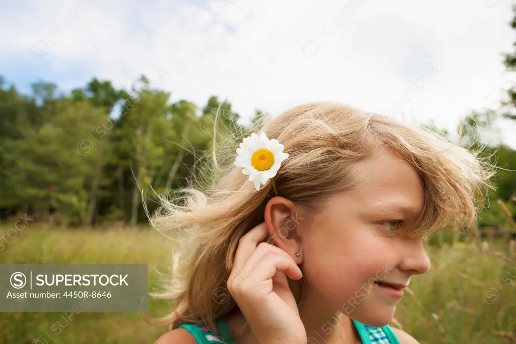 A young girl in the open air, with a daisy like flower behind her ear. New York state, USA. 6/26/2012