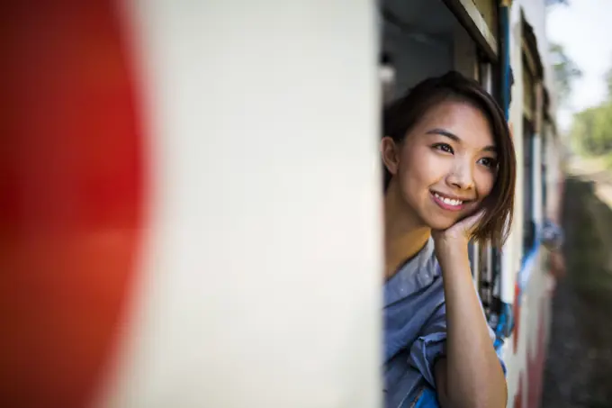 Smiling young woman riding on a train, looking out of window.