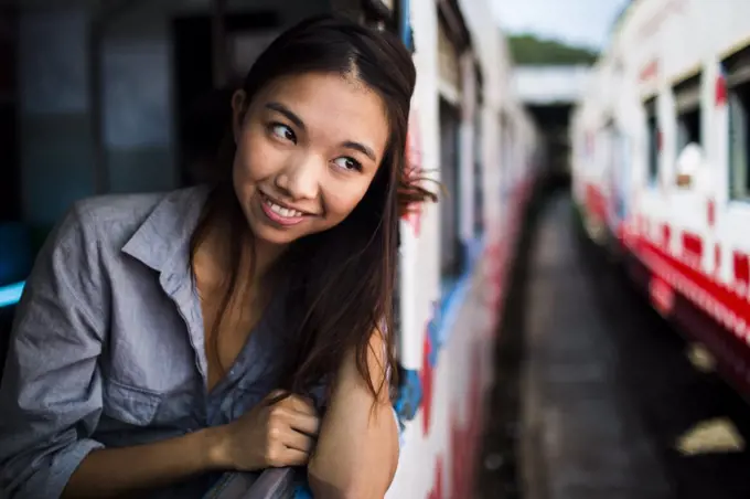 Smiling young woman riding on a train, looking out of window.