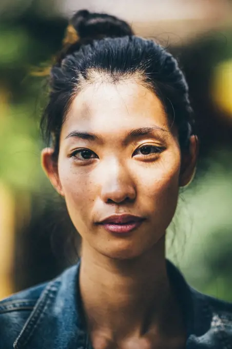 Portrait of a young woman with black hair tied in a top knot, looking at camera.