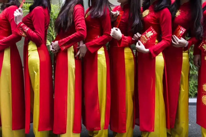 Close up of line of young women in traditional red and yellow dress outside of a wedding.