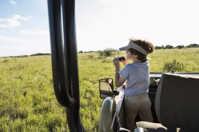 A six year old boy with binoculars in a safari vehicle