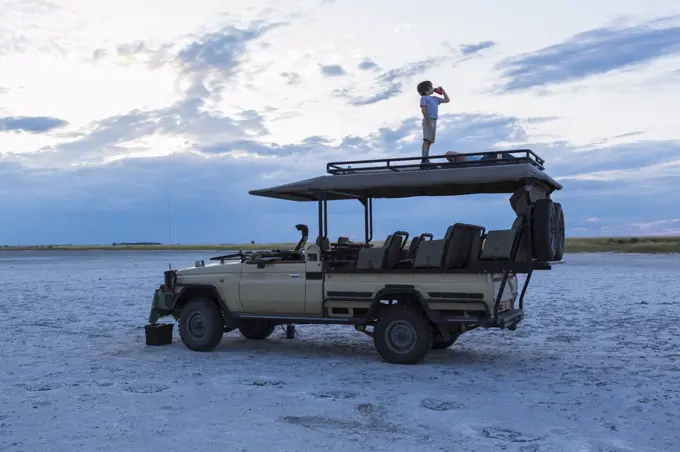 Six year old boy and older sister standing on top of safari vehicle, Nxai Pan, Botswana