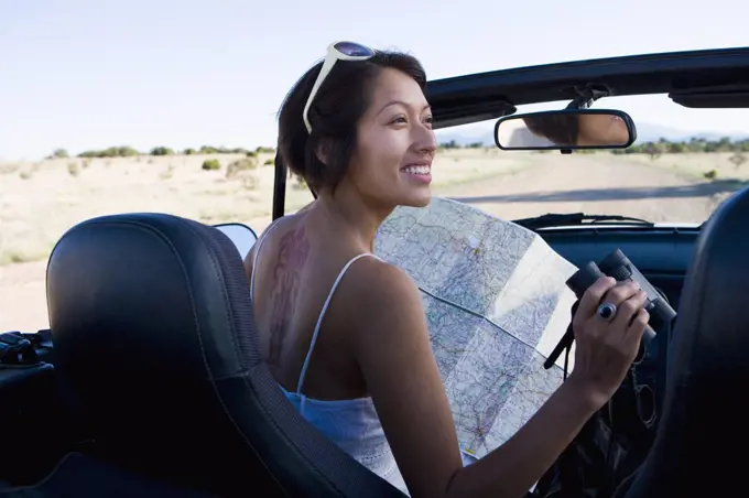 Native American woman in sun dress looking at a map in the passenger seat of a convertible.